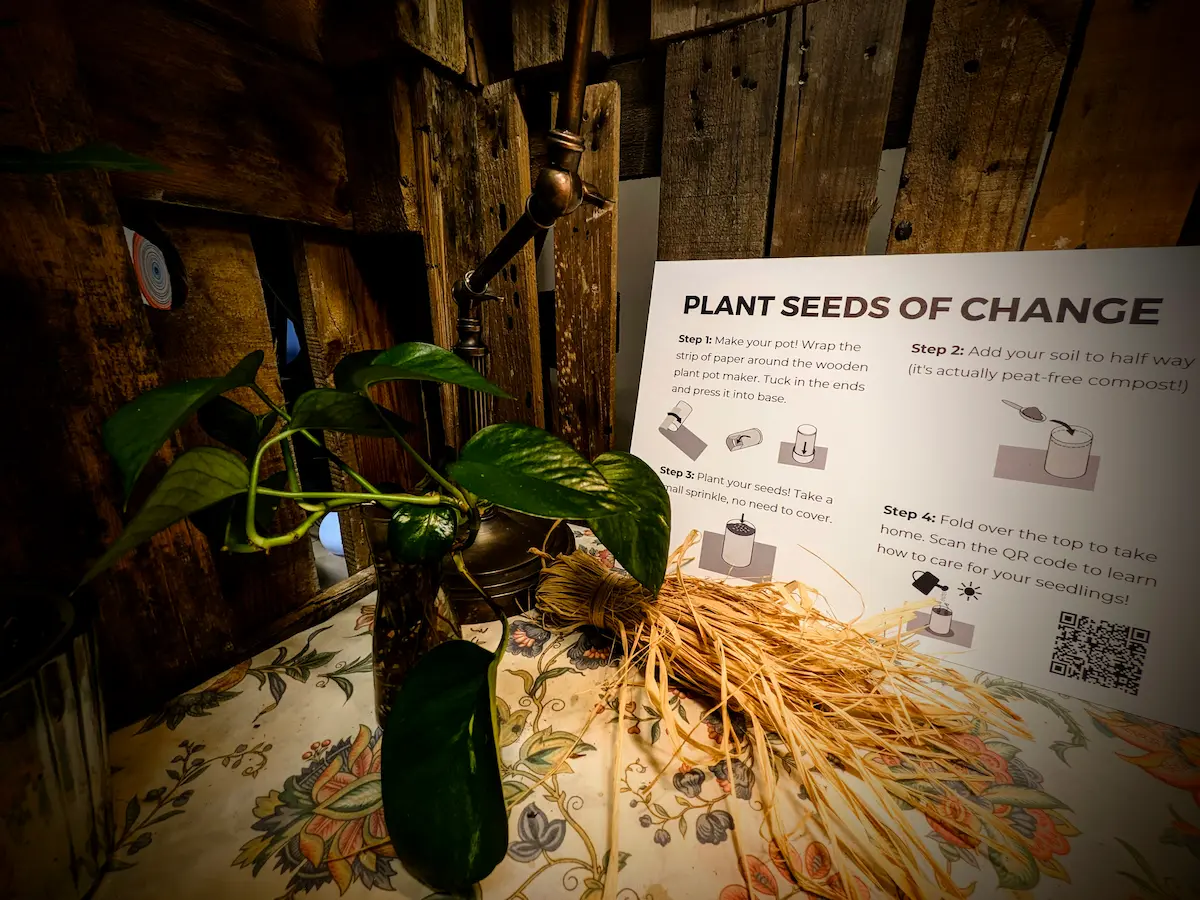 Interactive 'Plant Seeds of Change' exhibit with labeled plants, instructional signage, and organic materials.